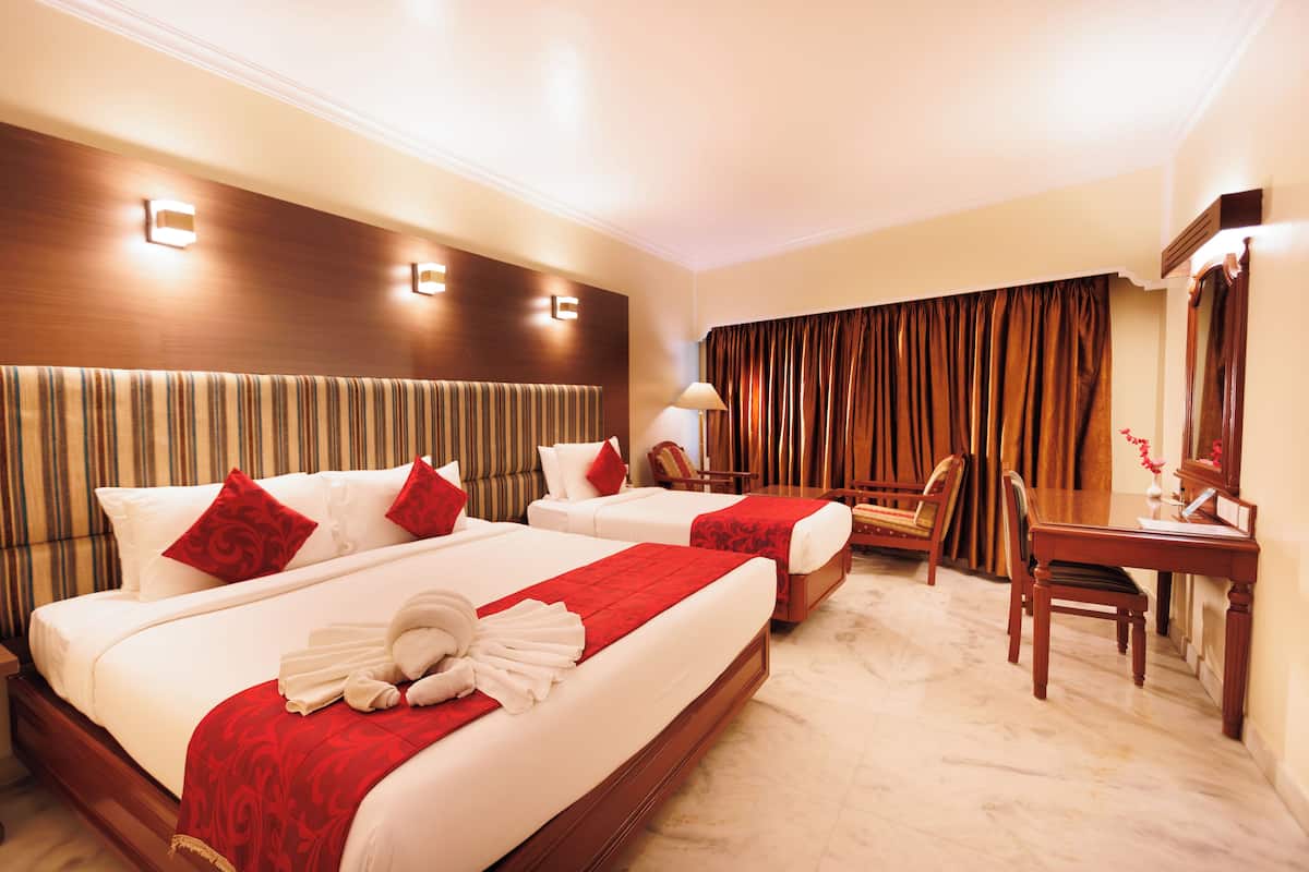 A hotel room with two beds, a desk, a chair, and a mirror.