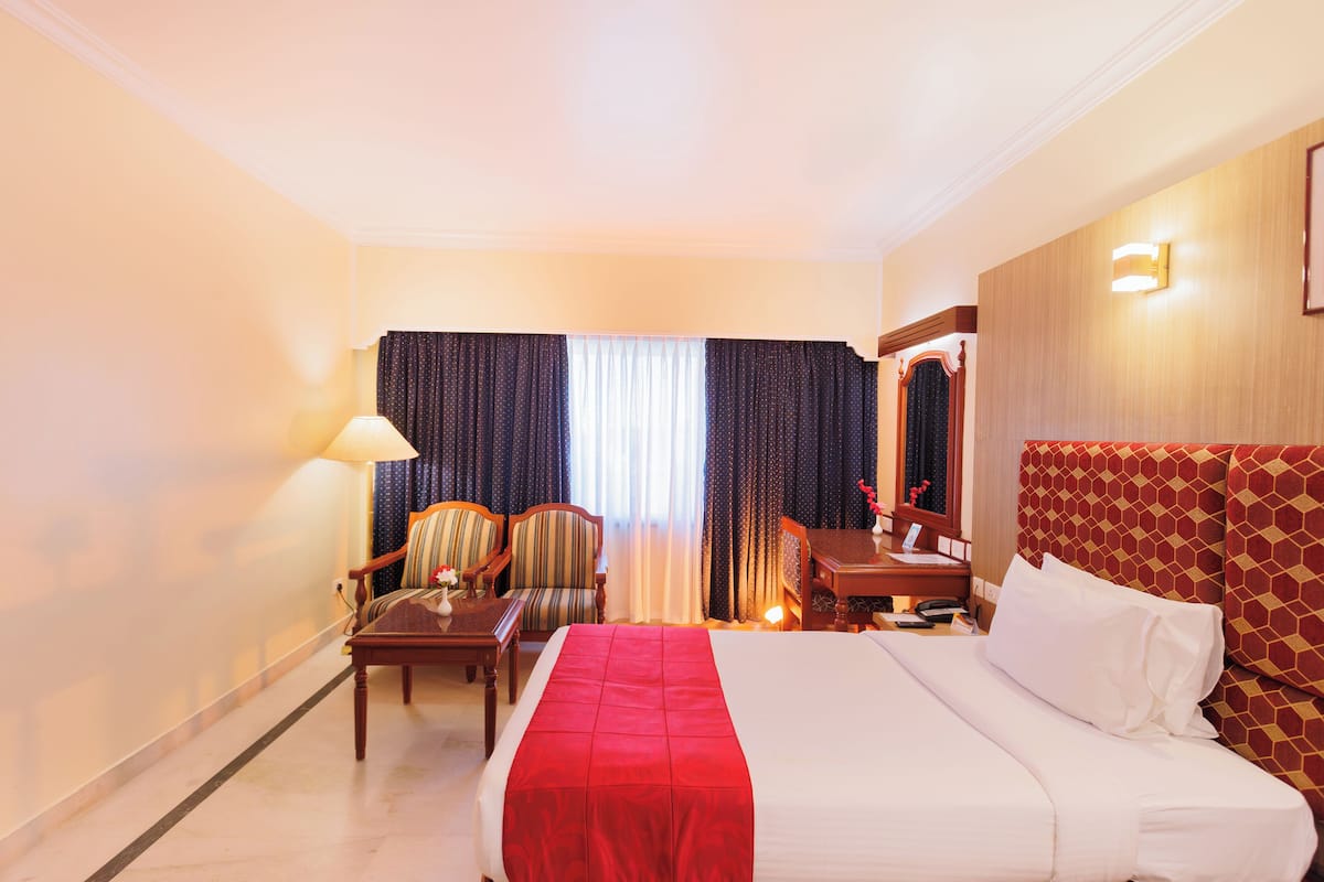 A hotel room with a large bed, a desk, a chair, and a lamp.