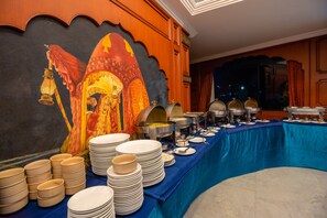 Tarjolla on runsas buffet, jossa on useita ruokapisteitä, seinällä on suuri seinämaalaus ja pöytä on peitetty sinisellä pöytäliinalla.