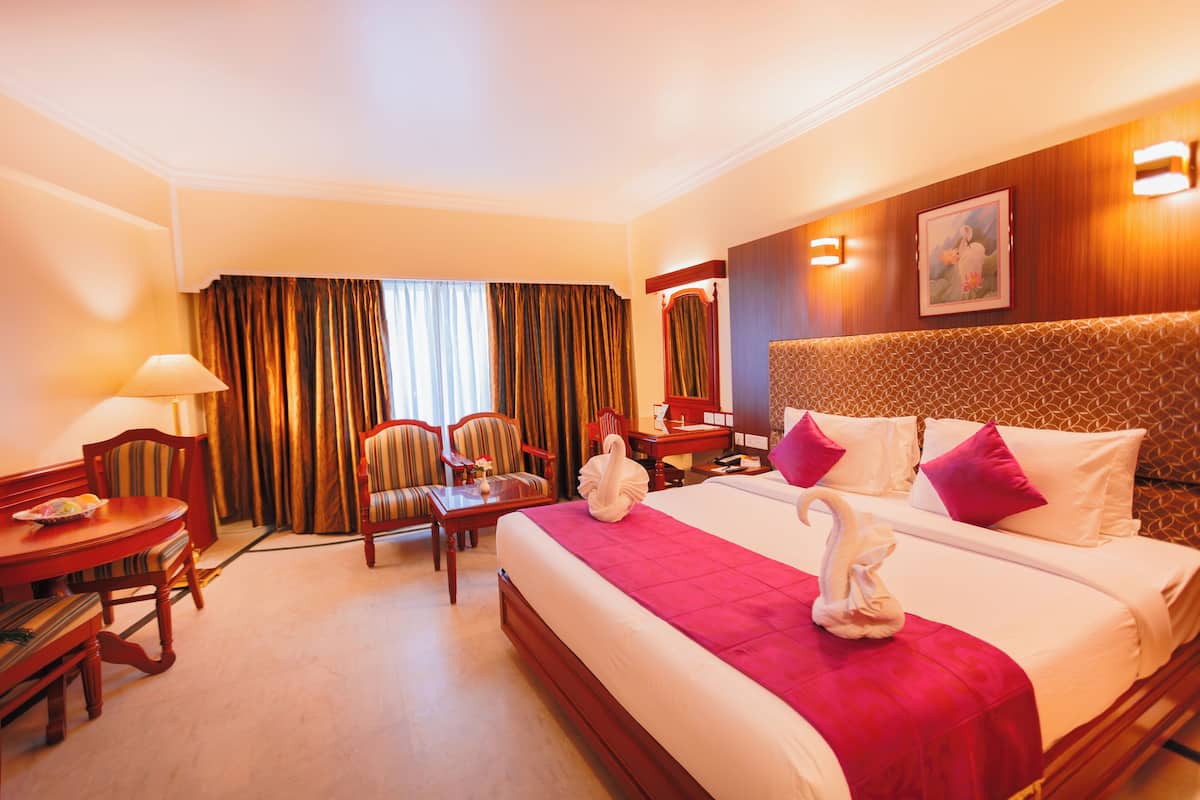 A hotel room with a large bed, a desk, a chair, a lamp, and a window with curtains.