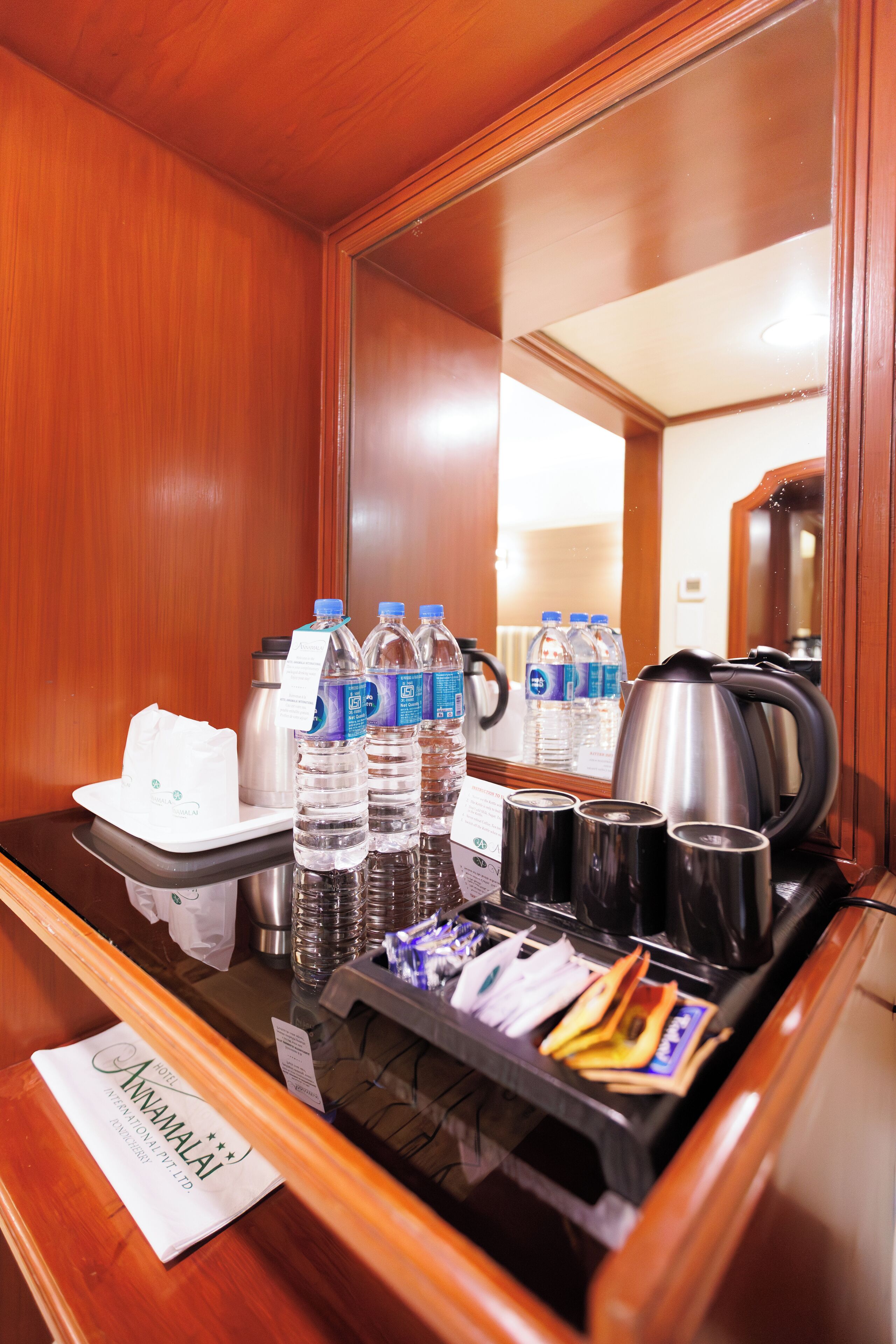 Un mini-bar dans la chambre d’hôtel contenant des bouteilles d’eau, une bouilloire et diverses collations.