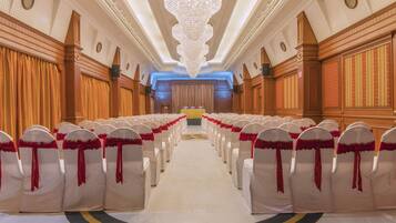 A hotel lobby with rows of white chairs with red sashes, a large chandelier, and wooden paneling on the walls.
