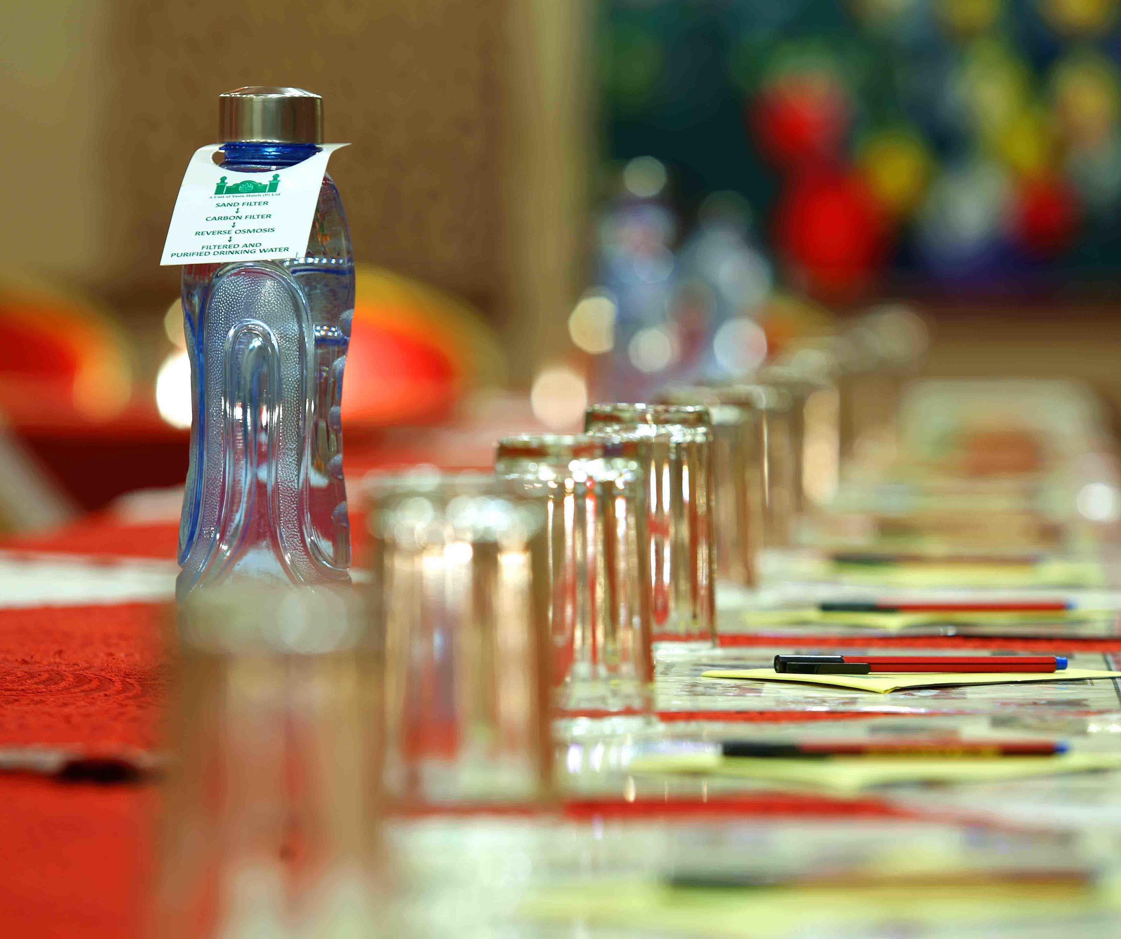 Eine Wasserflasche mit Etikett auf einem Tisch mit Gläsern und Stiften.