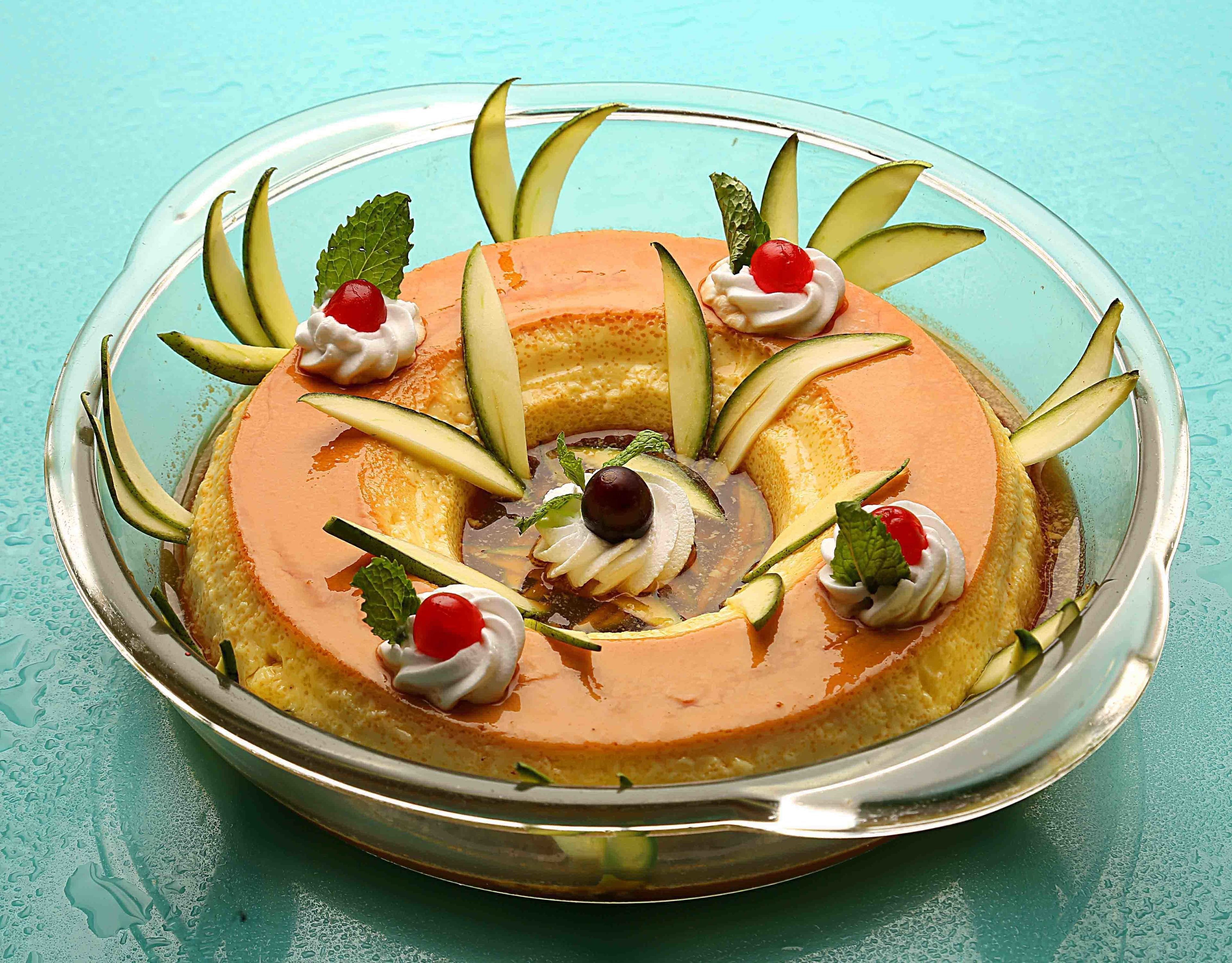 A round dessert with a caramelized top, garnished with mint leaves and cherries, on a clear glass plate.