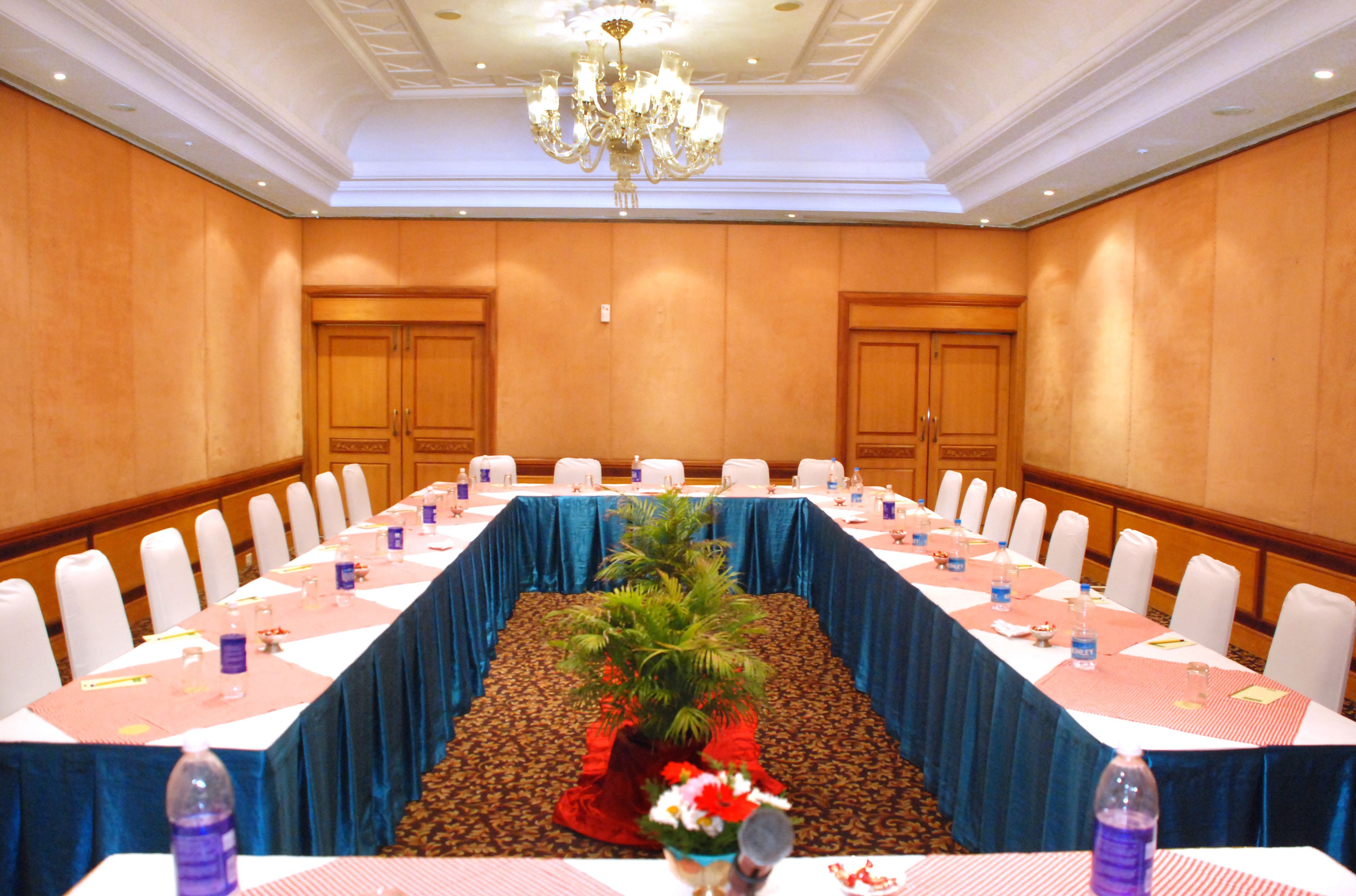 Un salón de conferencias con una larga mesa, sillas blancas y un mantel azul.