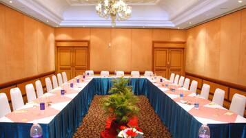 Un salón de conferencias con una larga mesa, sillas blancas y un mantel azul.