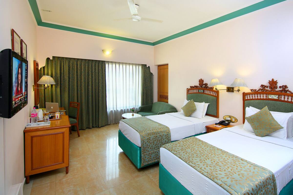 A hotel room with two beds, a desk with a computer, a TV, and a window with curtains.