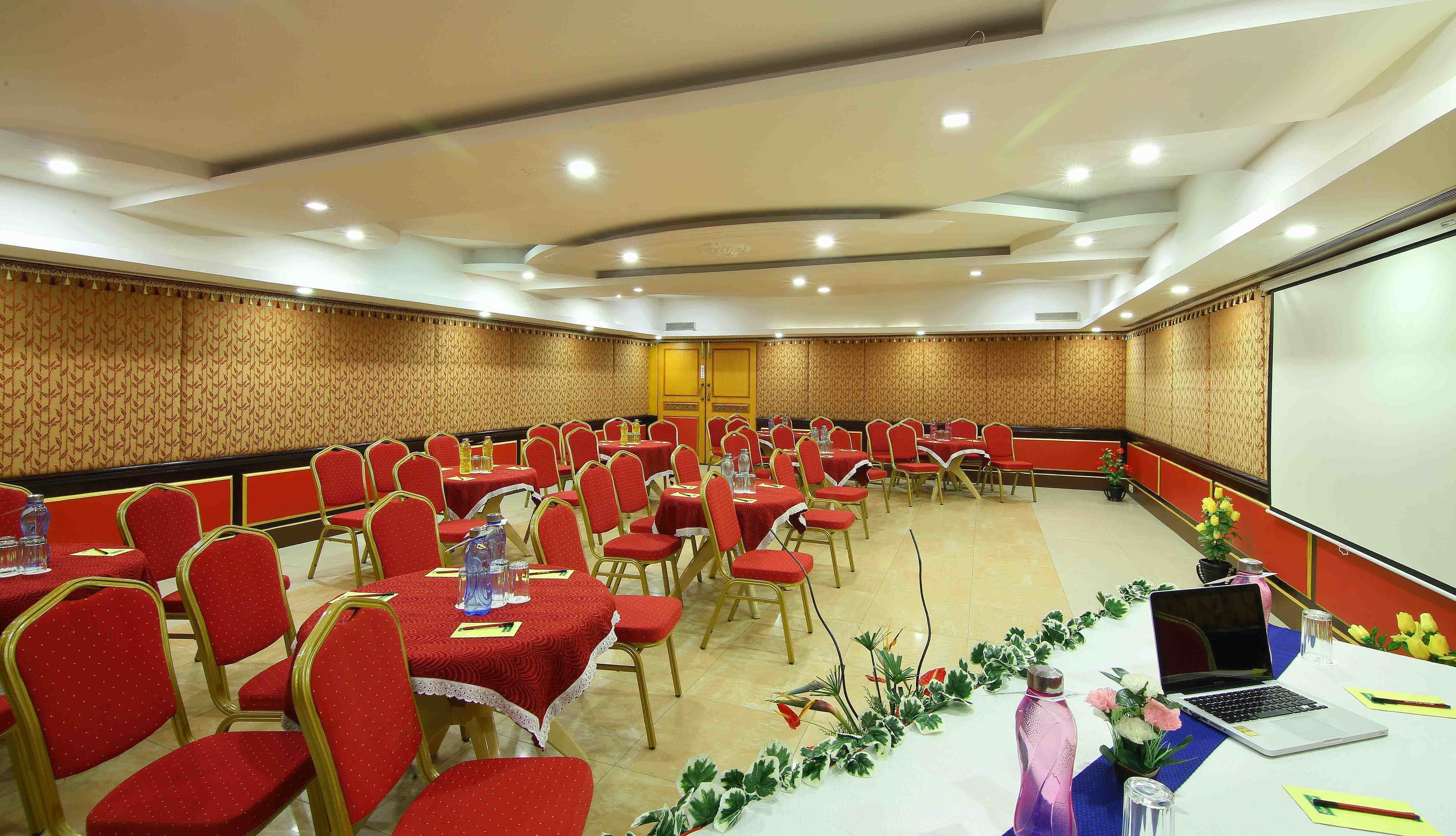 A conference room with red chairs and tables, equipped with water bottles and a laptop on the table.