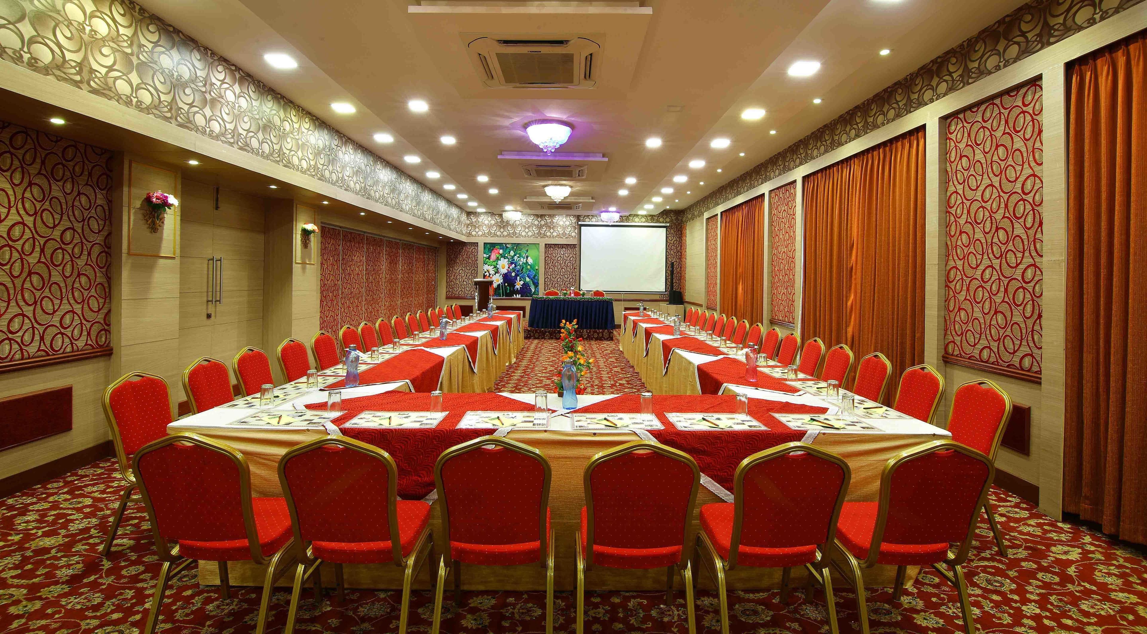 A conference room with a long table, red chairs, and a projector screen at the front.