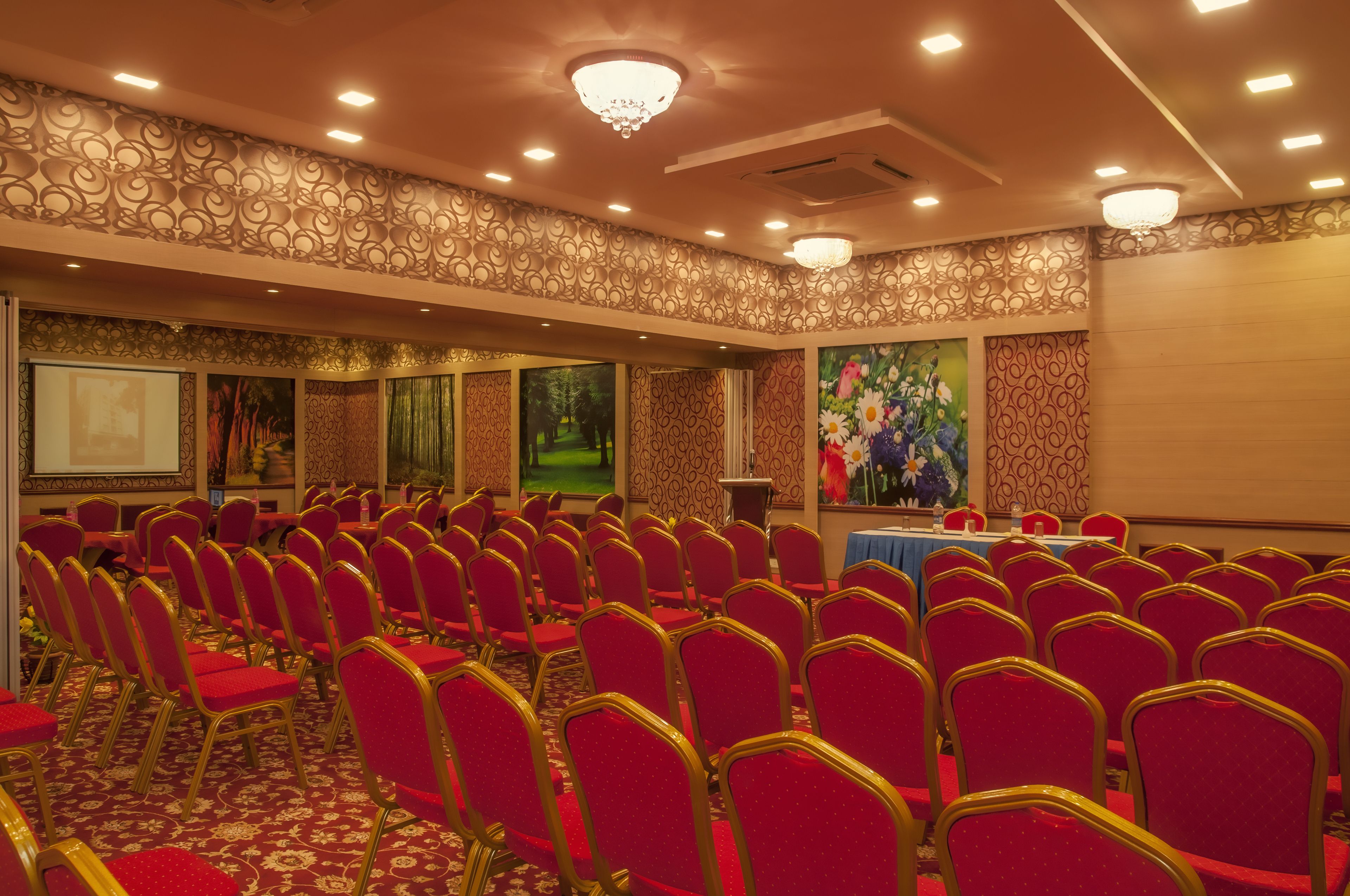 A conference room with rows of red chairs and tables, ornate wall designs, and a chandelier.