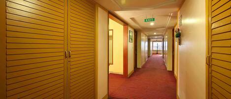 Un pasillo de hotel con puertas de madera, alfombra roja y señal de salida.