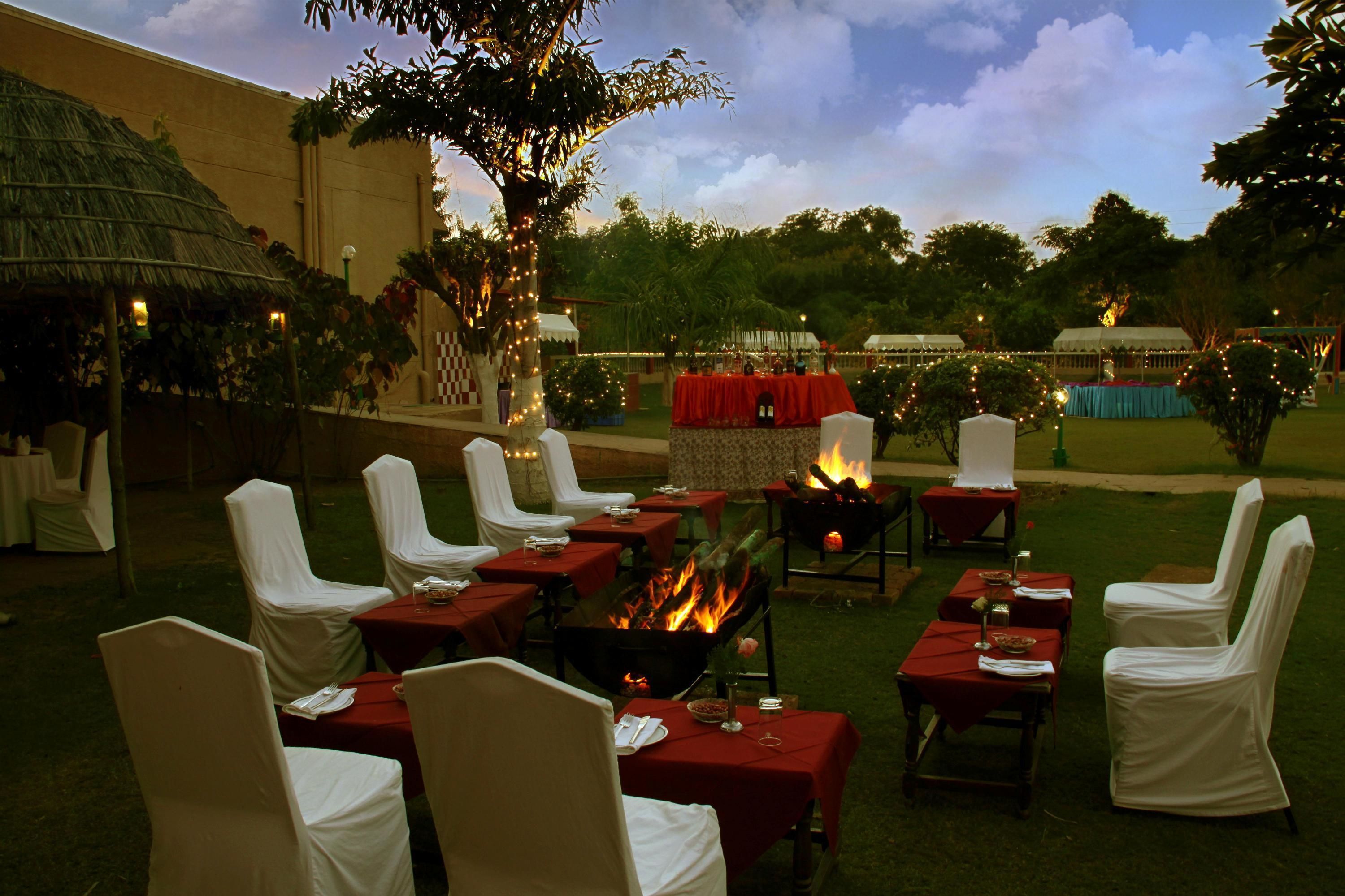 An outdoor dining area with tables and chairs, a fire pit, and a thatched-roof structure.