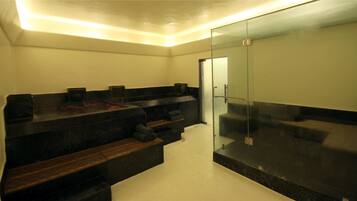 A modern bathroom with a glass shower enclosure, dark marble countertops, and wooden benches.