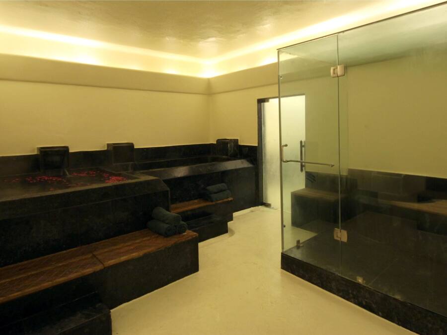 A modern bathroom with a glass shower enclosure, dark marble countertops, and wooden benches.