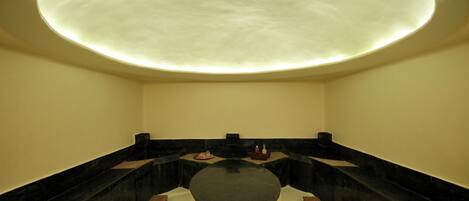 A modern spa room with a circular seating area, black marble steps, and a recessed ceiling light.