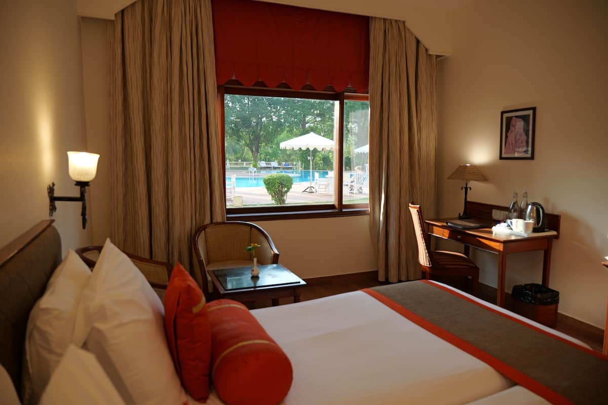 A hotel room with a bed, a desk, a chair, a lamp, and a window with a view of an outdoor area.