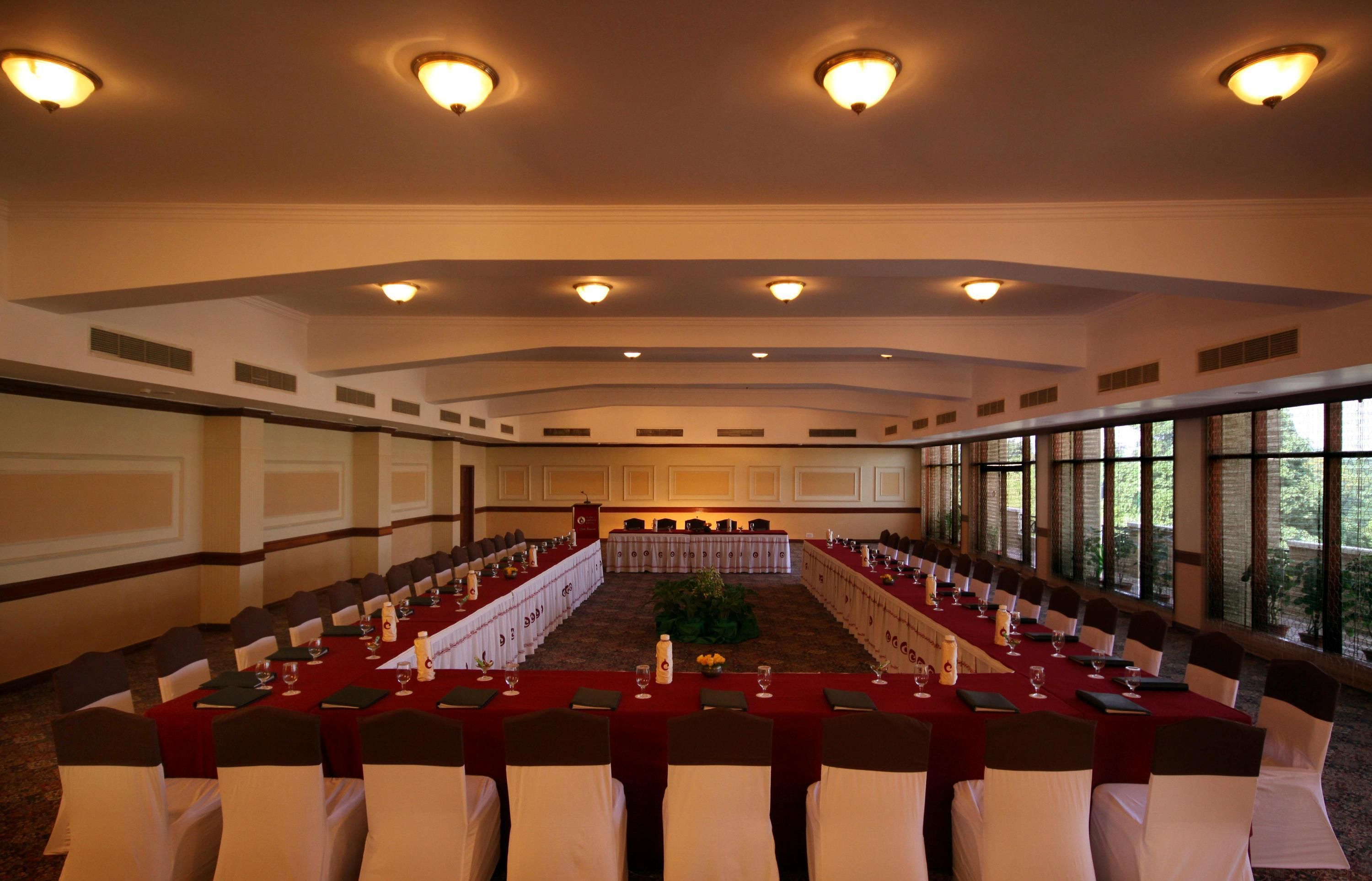 Un salón de conferencias con largas mesas, sillas blancas y piso alfombrado.