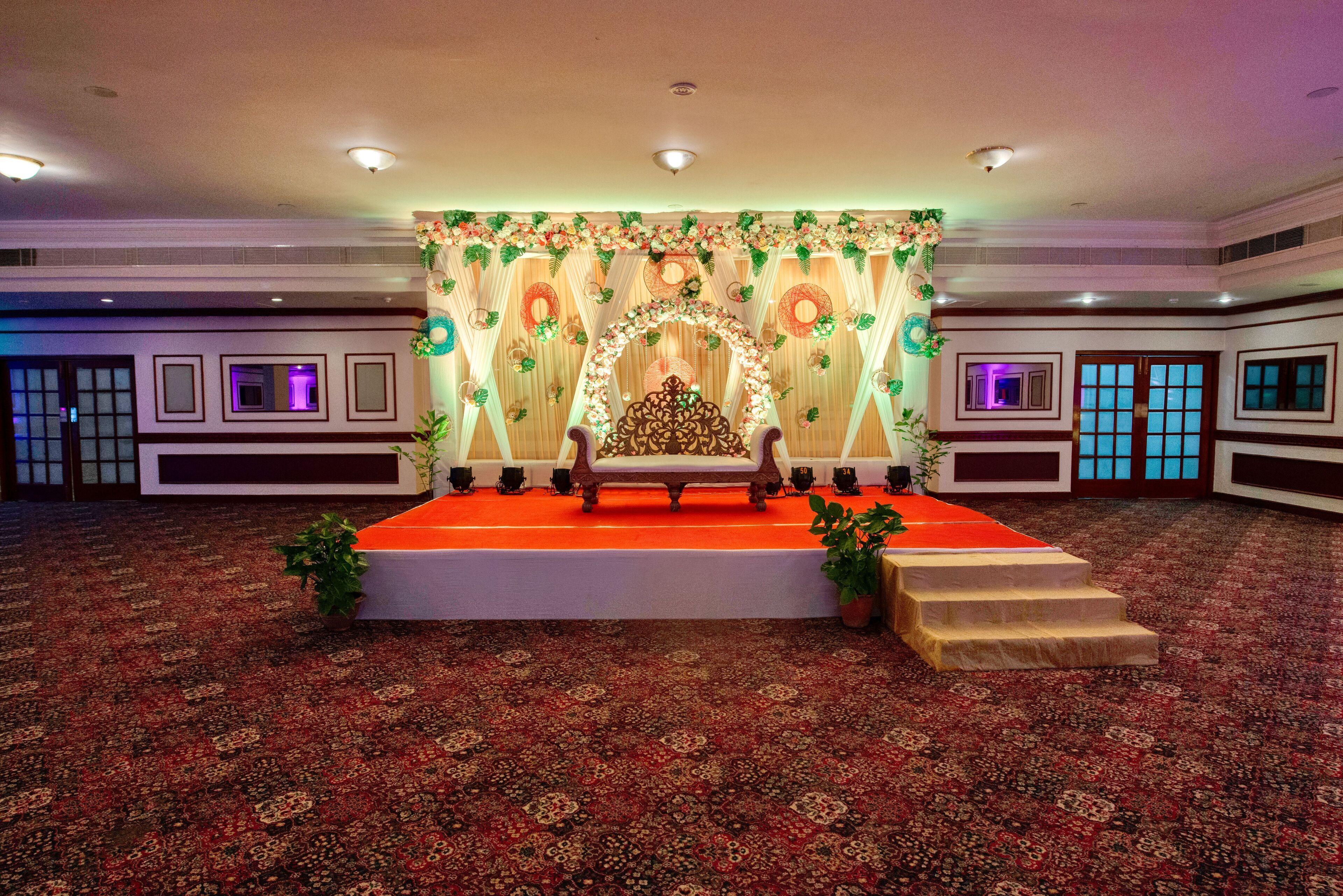 A stage with a floral backdrop, a red carpet, and a wooden bench.