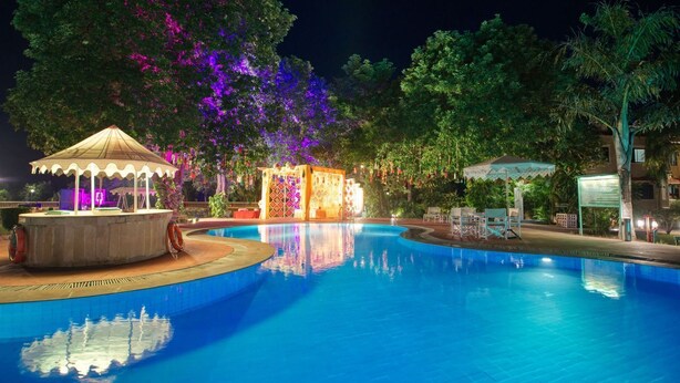 A nighttime swimming pool area with a gazebo, a decorative structure, and surrounding greenery. - Clarks Khajuraho (Rajnagar)