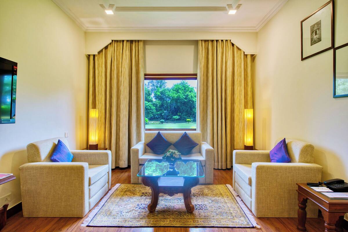 A room with two sofas facing a glass coffee table, a window with curtains, and a wooden floor.