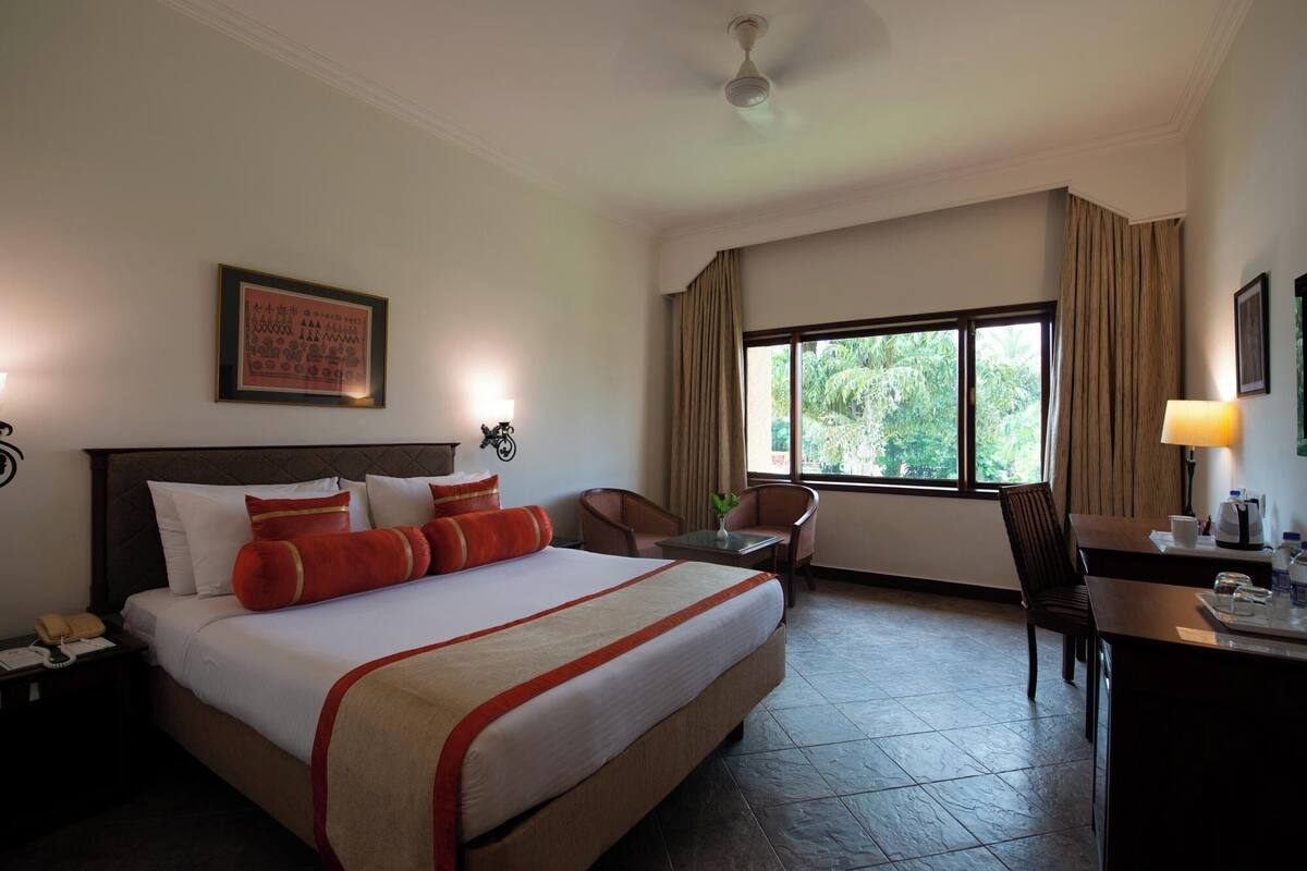 A hotel room with a large bed, a desk, a chair, a window with curtains, and a ceiling fan.