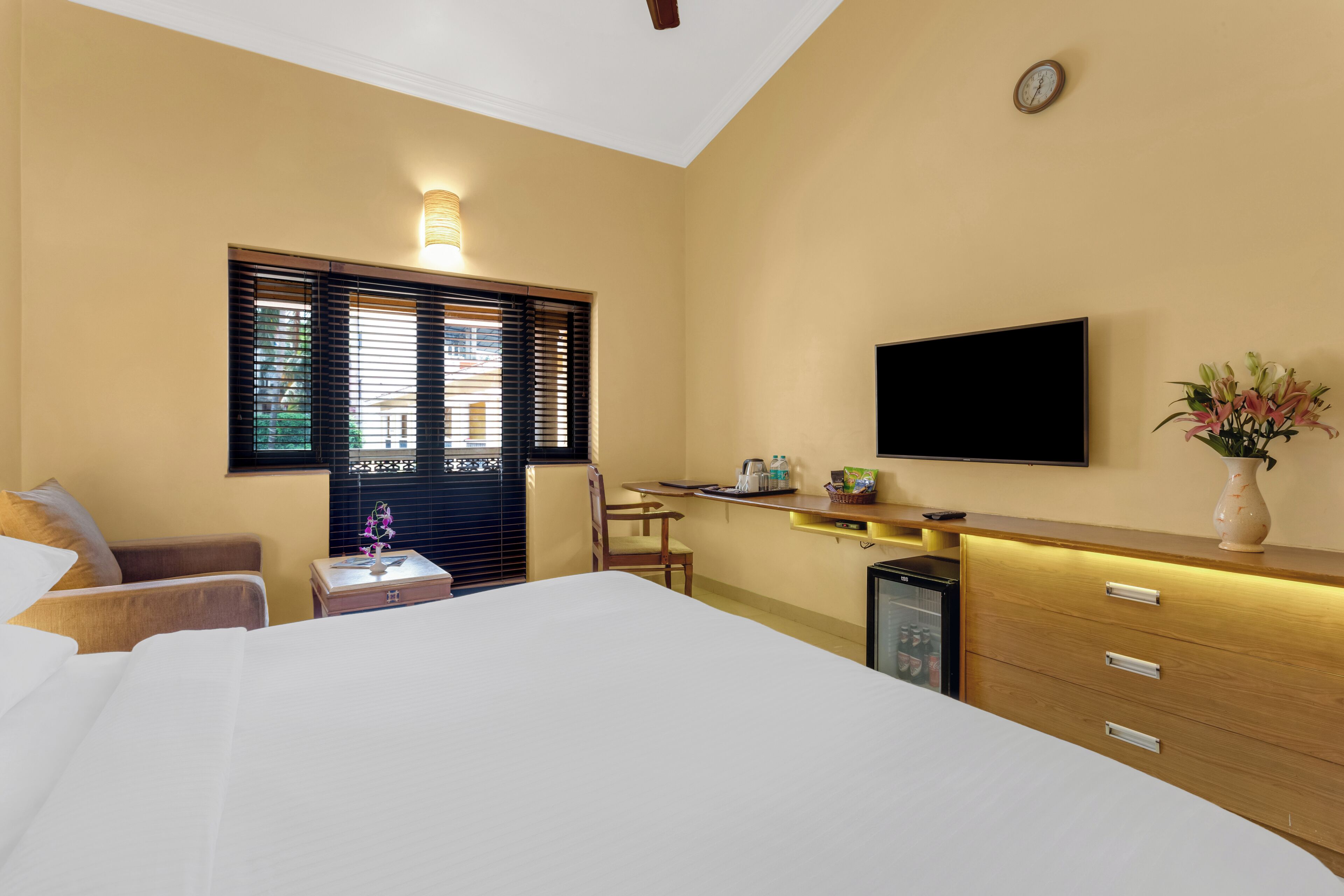 A hotel room with a bed, a desk with a chair, a television, and a minibar.