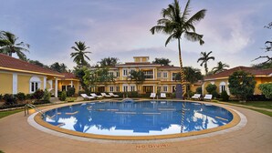 A large pool surrounded by palm trees and a building with a tiled roof. - Casa De Goa Boutique Resort (Calangute)