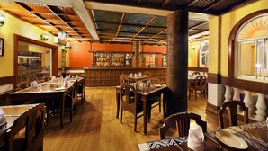 A restaurant interior with wooden tables and chairs, a bar area, and a large pillar. - Casa De Goa Boutique Resort (Calangute)