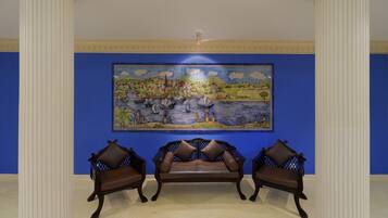 Une pièce avec un mur bleu, un grand tableau représentant un paysage et deux canapés en cuir marron.