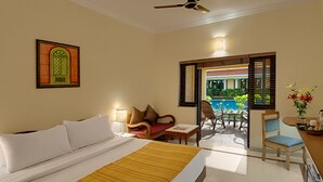 A hotel room with a bed, a desk, a chair, a table, a ceiling fan, and a view of a pool. - Casa De Goa Boutique Resort (Calangute)