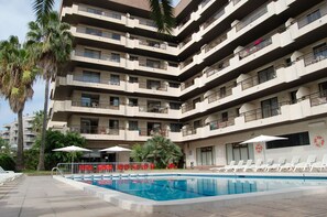 Un hôtel à plusieurs étages doté d’une piscine, d’un espace extérieur aménagé et de palmiers.