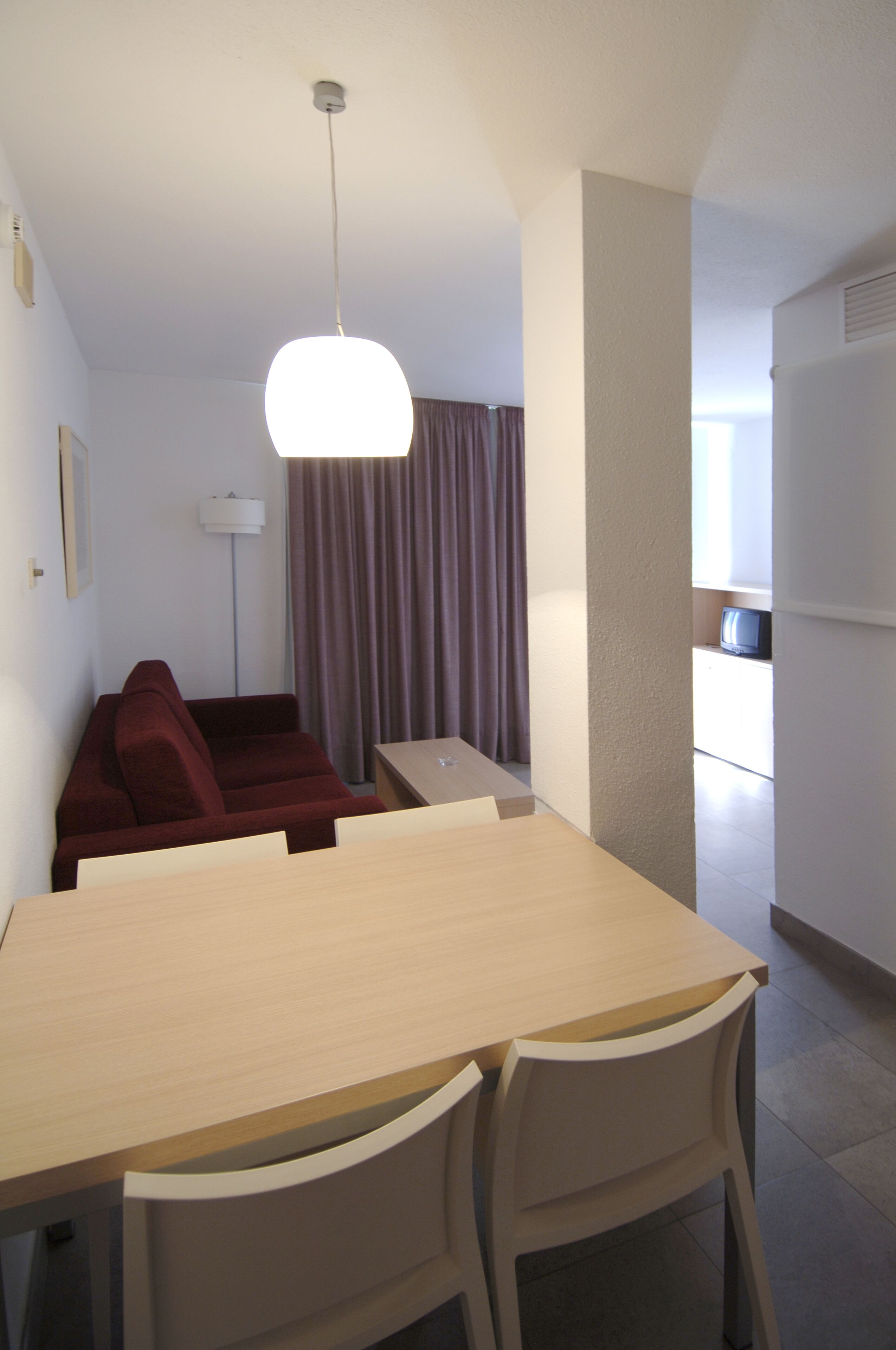 Un espacio habitable compacto con una mesa de comedor y sillas, un sofá rojo, una lámpara de pie y un televisor al fondo.