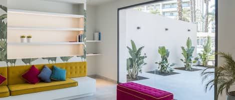 A modern interior with a yellow sofa, a pink ottoman, and a white shelving unit.