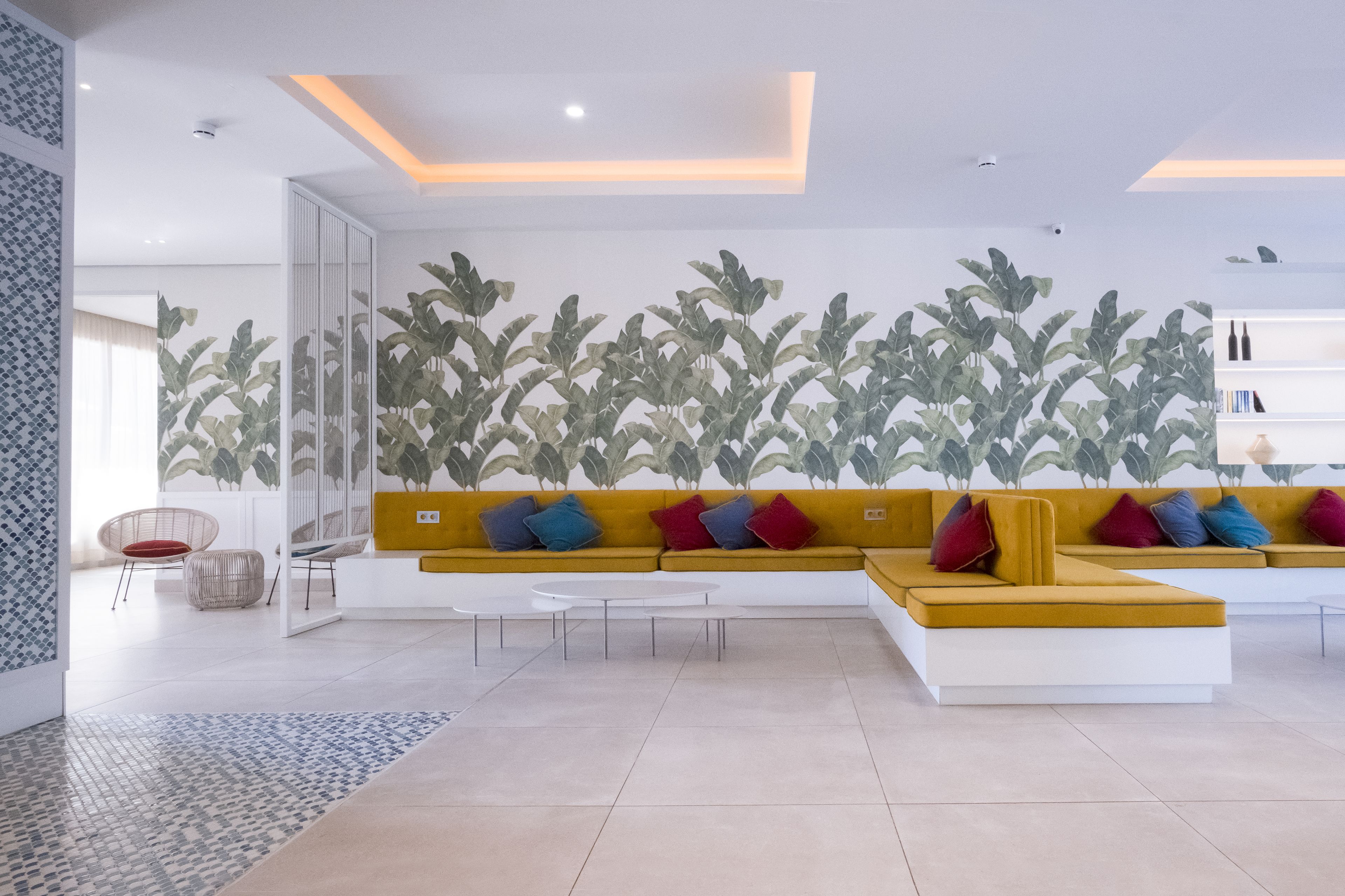 Una sala de estar moderna con un sofá amarillo, una mesa de centro blanca y una pared decorativa con motivos de hojas.
