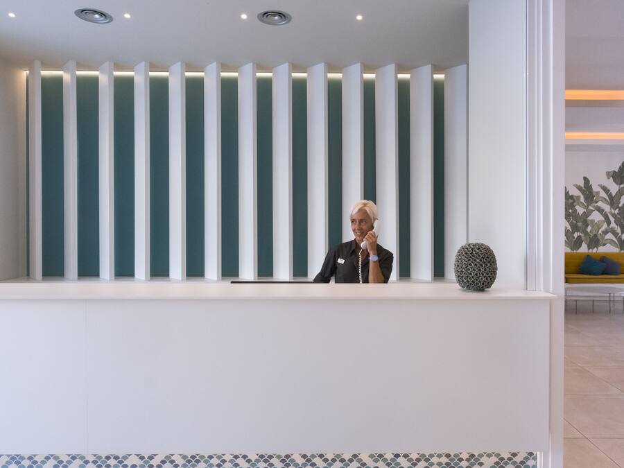 Un mostrador de recepción con paneles de luz verticales, una recepcionista y un jarrón decorativo.