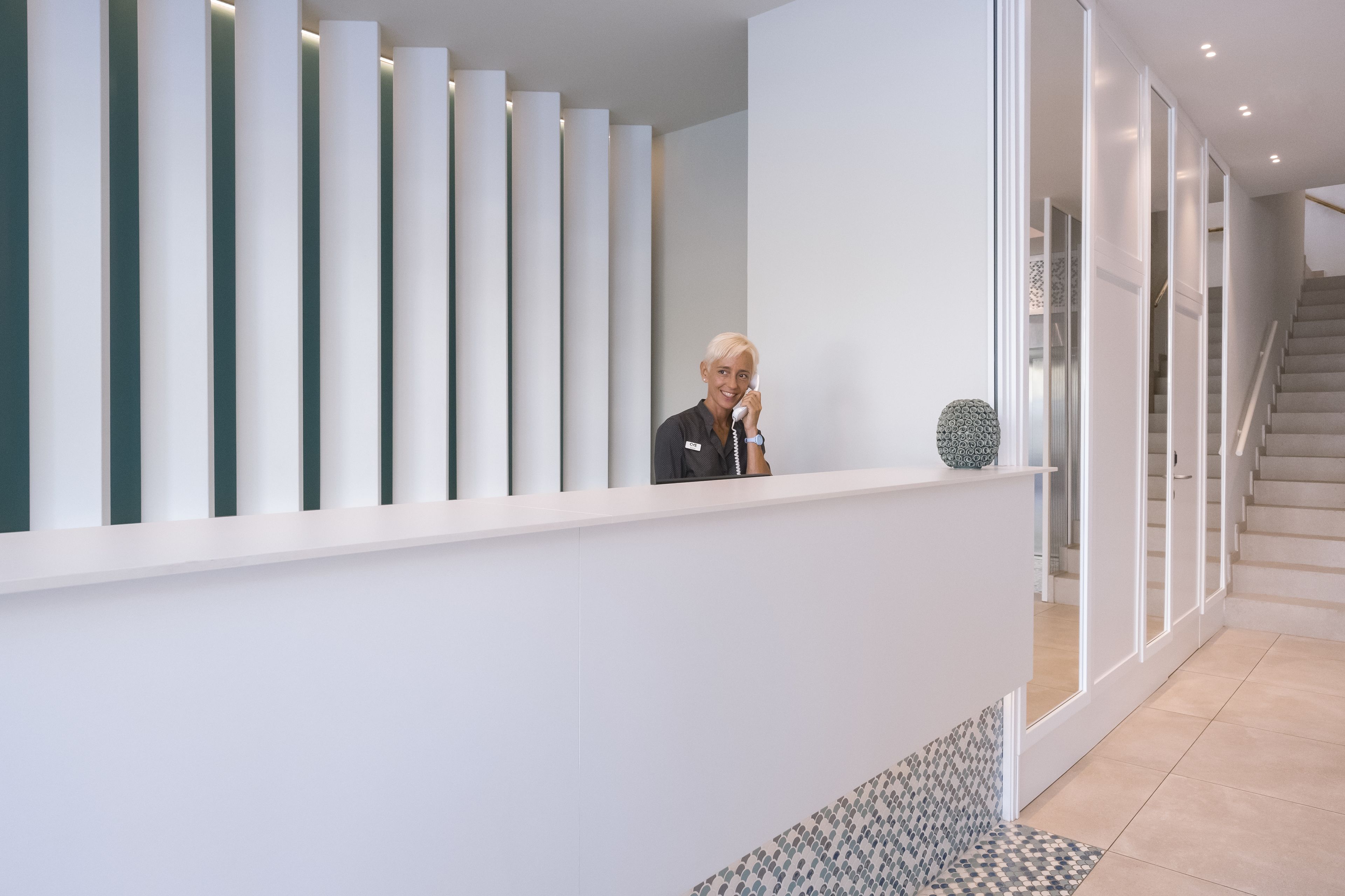 Un espace d’accueil moderne avec un comptoir d’accueil blanc, un escalier et un sol à motifs.