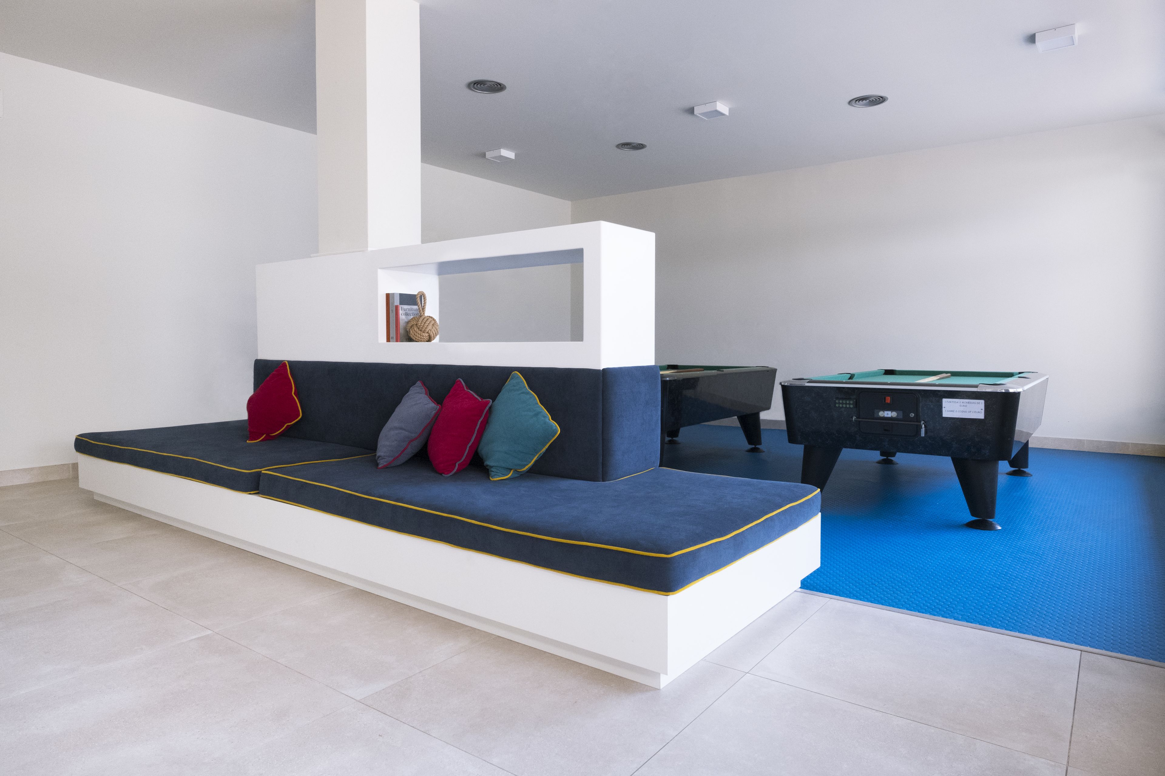A modern living room with a sofa, a pool table, and a blue carpet.