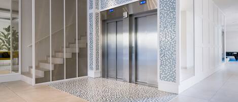 A modern elevator with a digital display, a patterned floor, and a staircase with a glass railing.