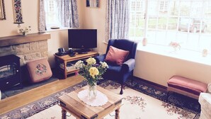 A cozy living room with a fireplace, a television, a comfortable armchair, and a large window offering a view of the outside. - Lastingham Grange (York)