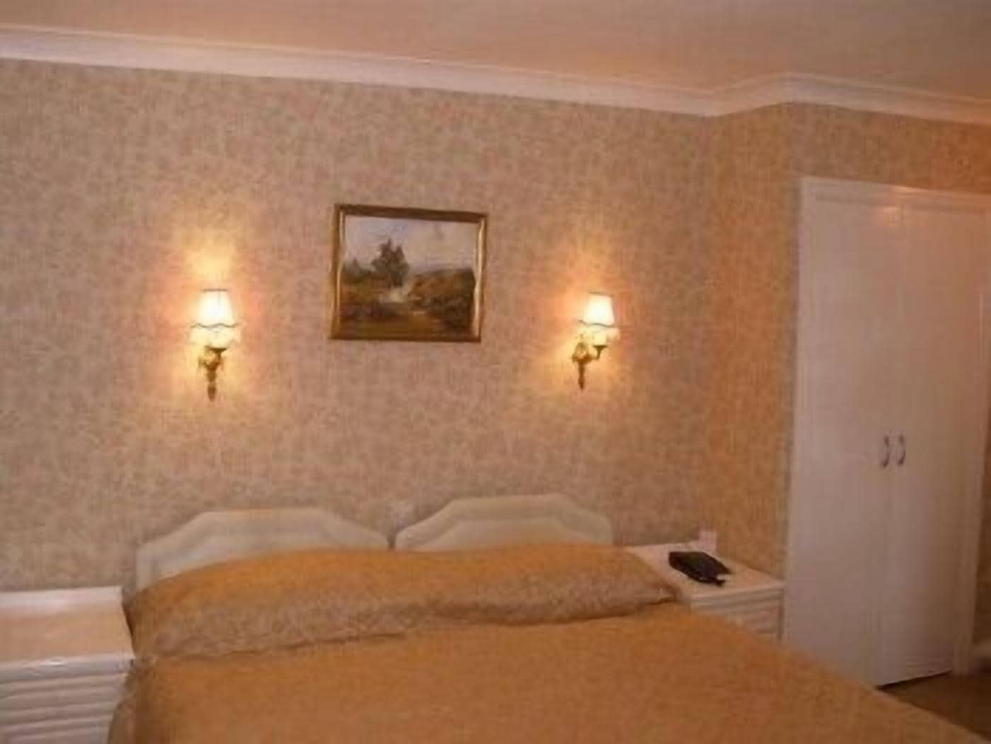 Un dormitorio con cama, dos lámparas de pared, un cuadro enmarco y una puerta blanca.