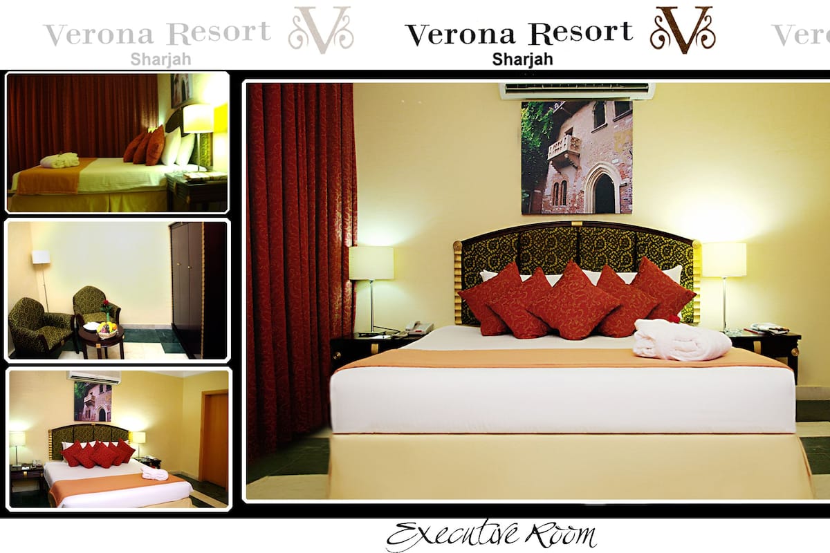 Habitación de hotel con una cama grande, cabecera con diseños decorativos, televisor de pantalla plana, escritorio con silla y zona de comedor con mesa y sillas.