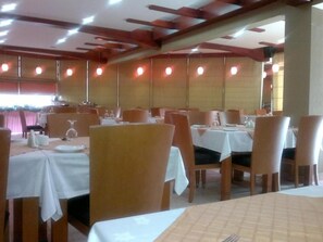 Un restaurant amb diverses taules i caires, algunes amb tovallols blancs.