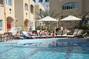 Zona de piscina amb gandules i ombrelles, envoltada d'un edifici amb finestres d'arc i una piscina amb vora de rajola.