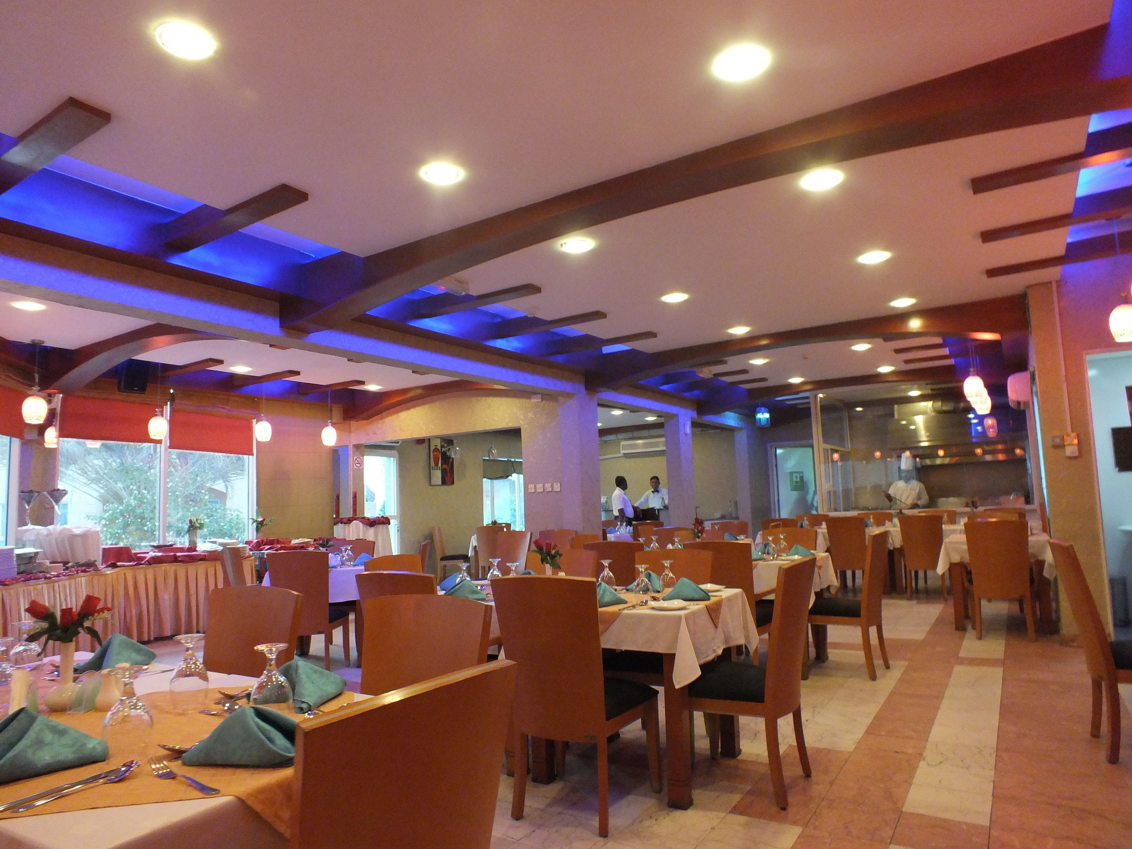A restaurant with tables set for dining, wooden chairs, and a ceiling with exposed beams and recessed lighting.