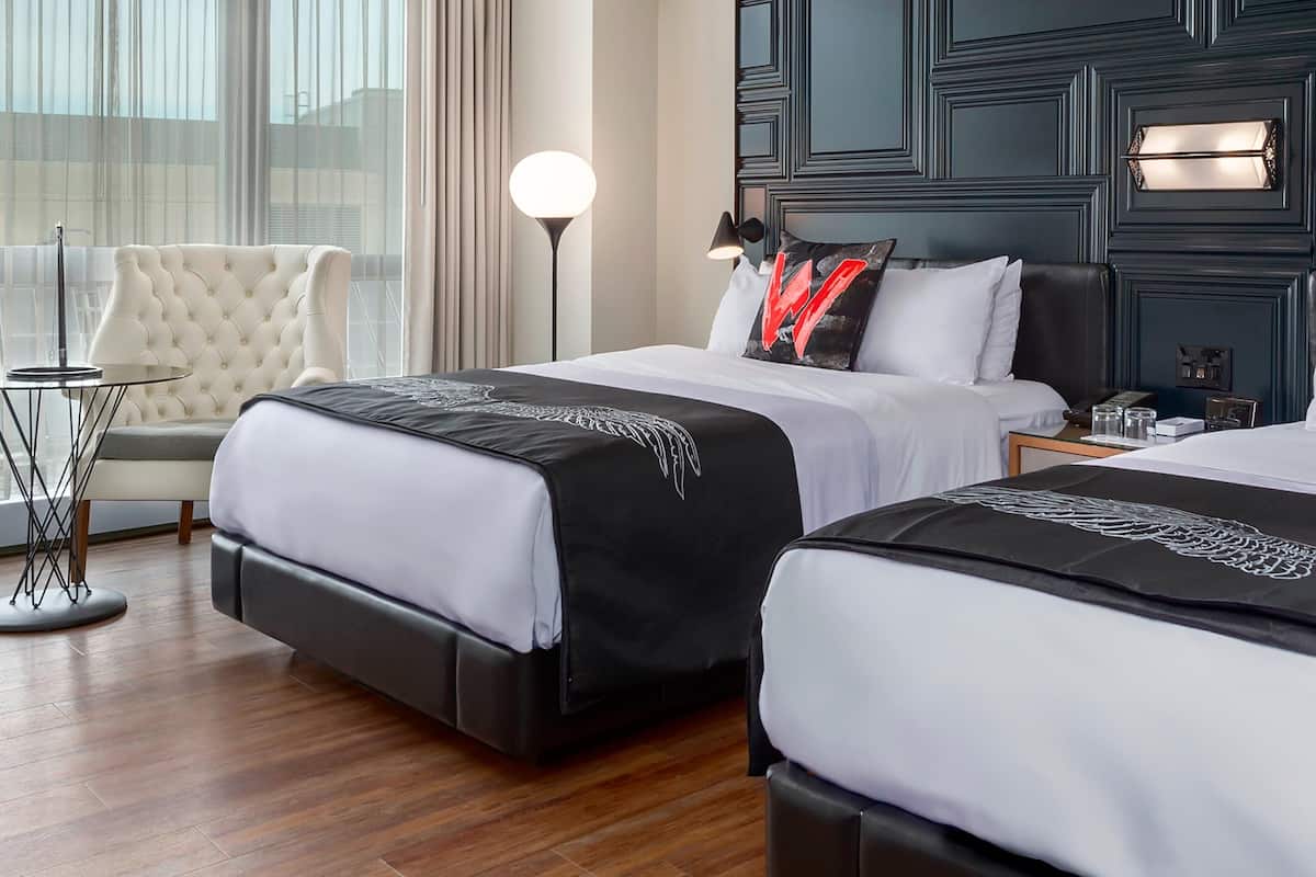 Een hotelkamer met twee bedden, een witte fauteuil, een kleine ronde tafel en een vloerlamp.