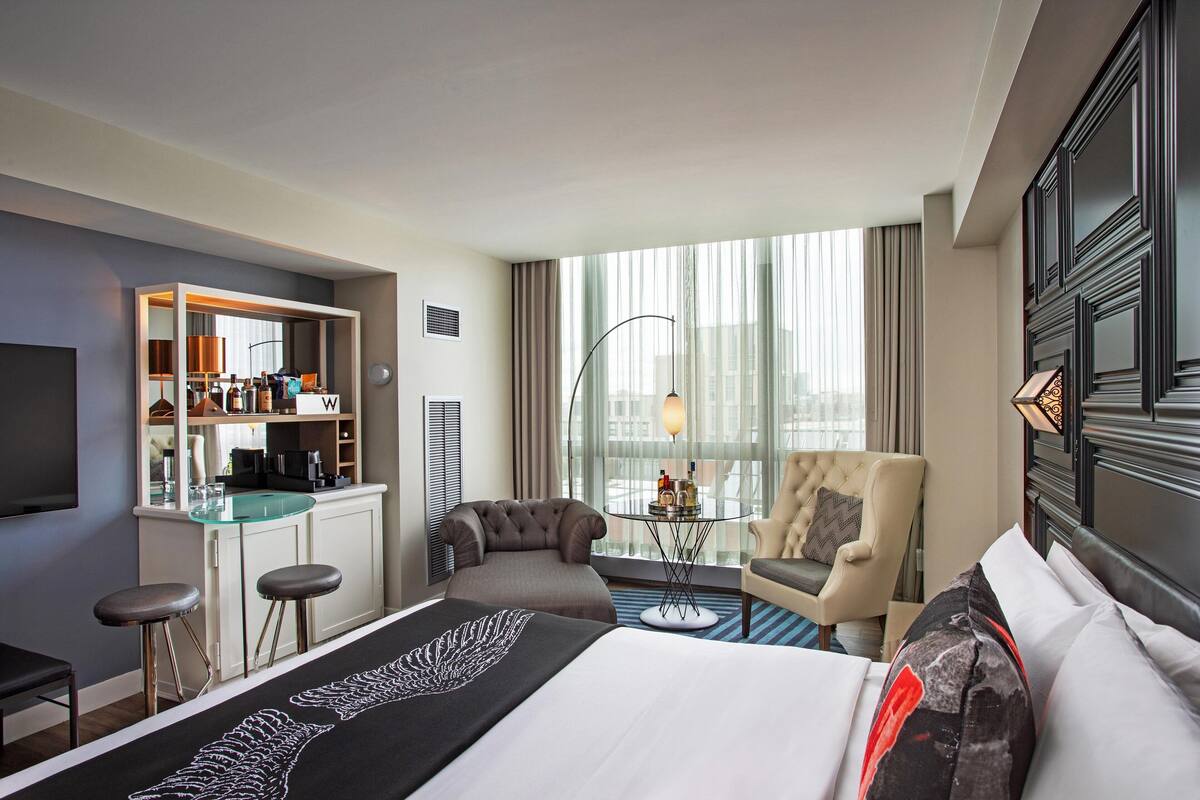 Een hotelkamer met een bed, twee fauteuils, een klein tafeltje met drankjes, een televisie en een minibars.