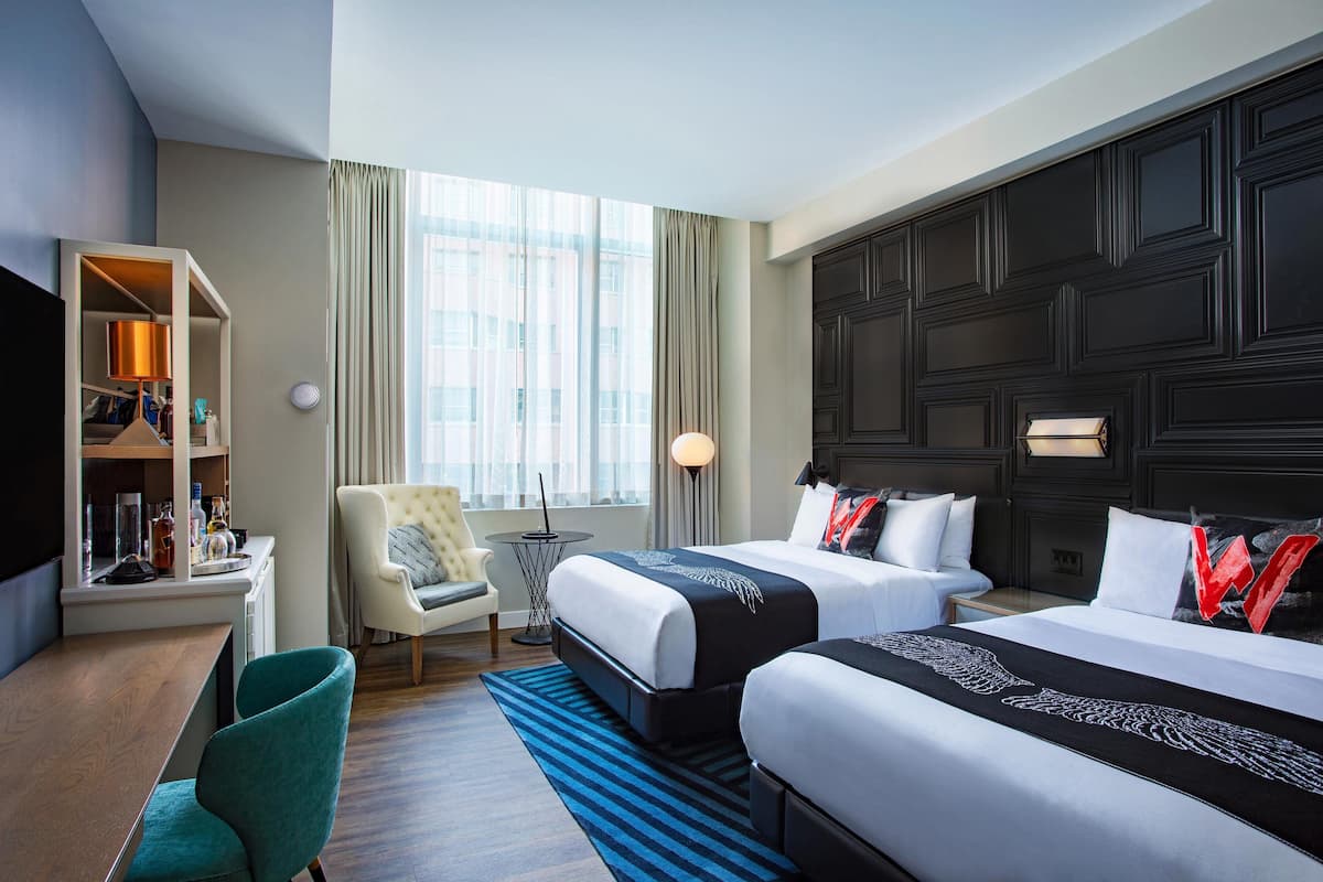 Een hotelkamer met twee bedden, een bureau met stoel, een televisie en een groot raam met gordijnen.