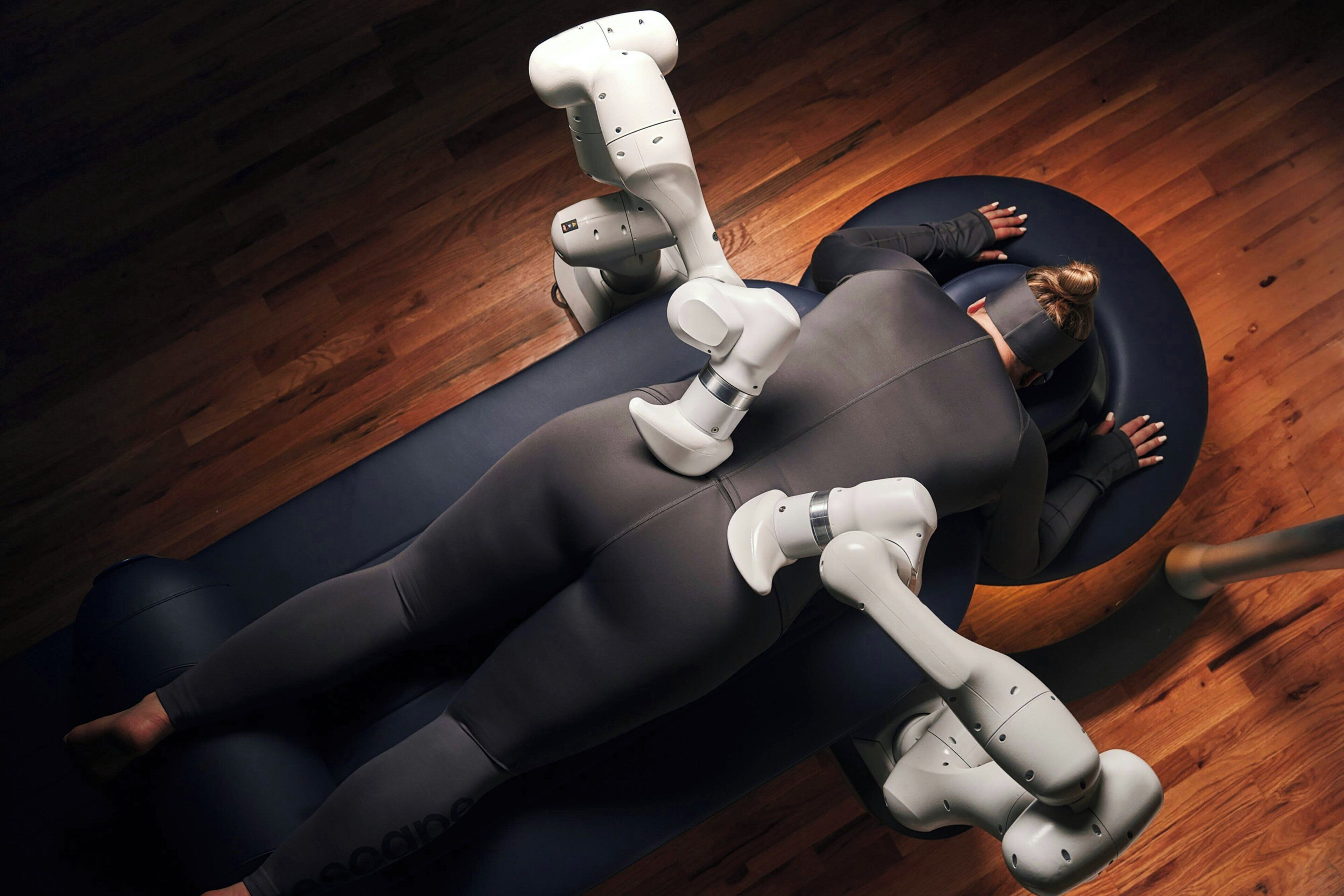 A person lying on a dark-colored couch with a robotic arm positioned above them.