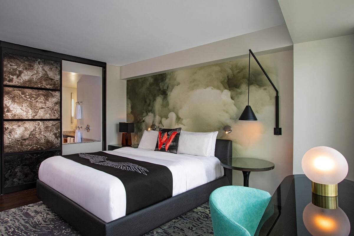Een moderne hotelkamer met een groot bed, een ronde tafel, een blauwgroene stoel en een uniek kunstwerk aan de muur.
