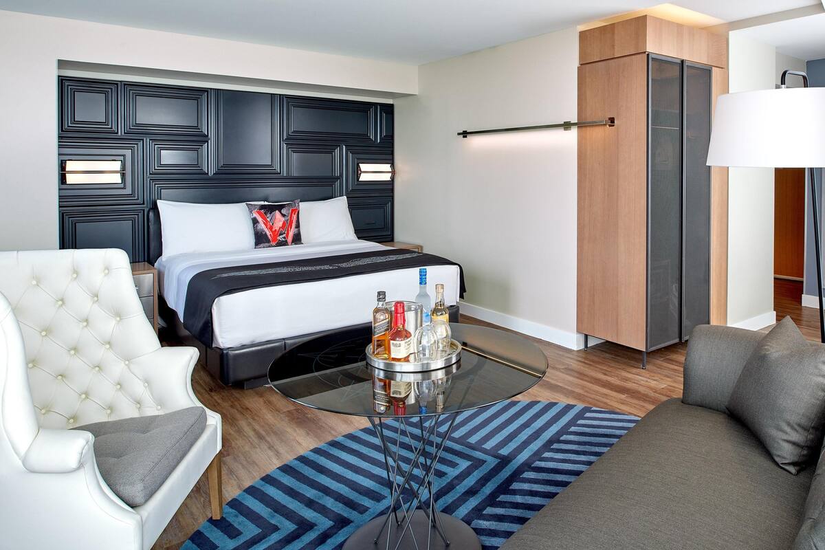 Een moderne hotelkamer met een groot bed, een gestoffeerde fauteuil, een bank, een glazen bijzettafeltje en een minibar.